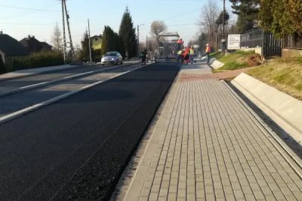 Zdjęcie przedstawiające układanie nowej nawierzchni asfaltowej obok chodnika z kostki brukowej..